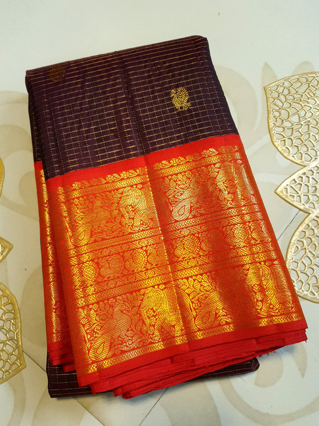 Dark plum Kanchipuram silk saree featuring a gold Muthukattam check pattern, ornate zari buttas, and a vibrant contrast border and pallu.