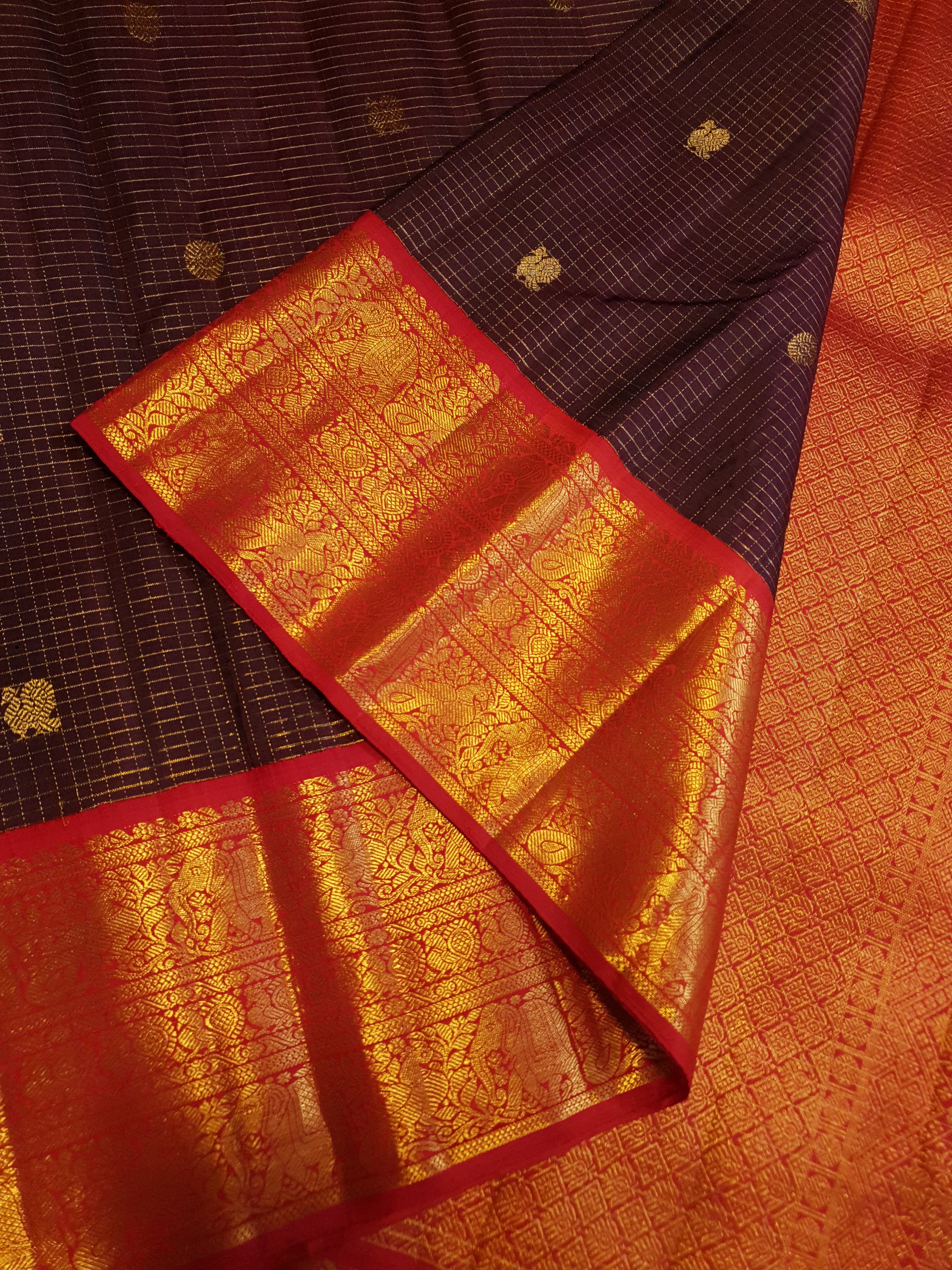 Dark plum Kanchipuram silk saree featuring a gold Muthukattam check pattern, ornate zari buttas, and a vibrant contrast border and pallu.