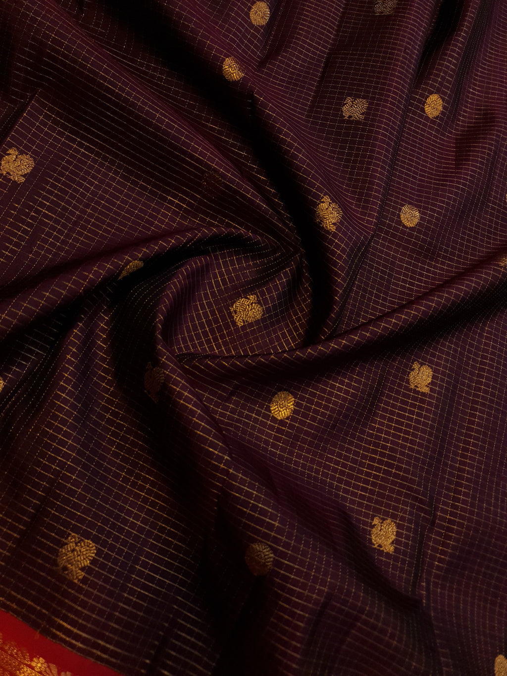 Dark plum Kanchipuram silk saree featuring a gold Muthukattam check pattern, ornate zari buttas, and a vibrant contrast border and pallu.