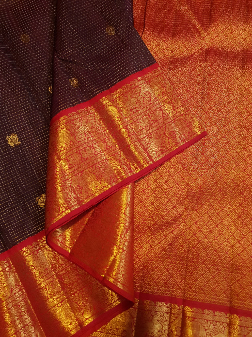 Dark plum Kanchipuram silk saree featuring a gold Muthukattam check pattern, ornate zari buttas, and a vibrant contrast border and pallu.