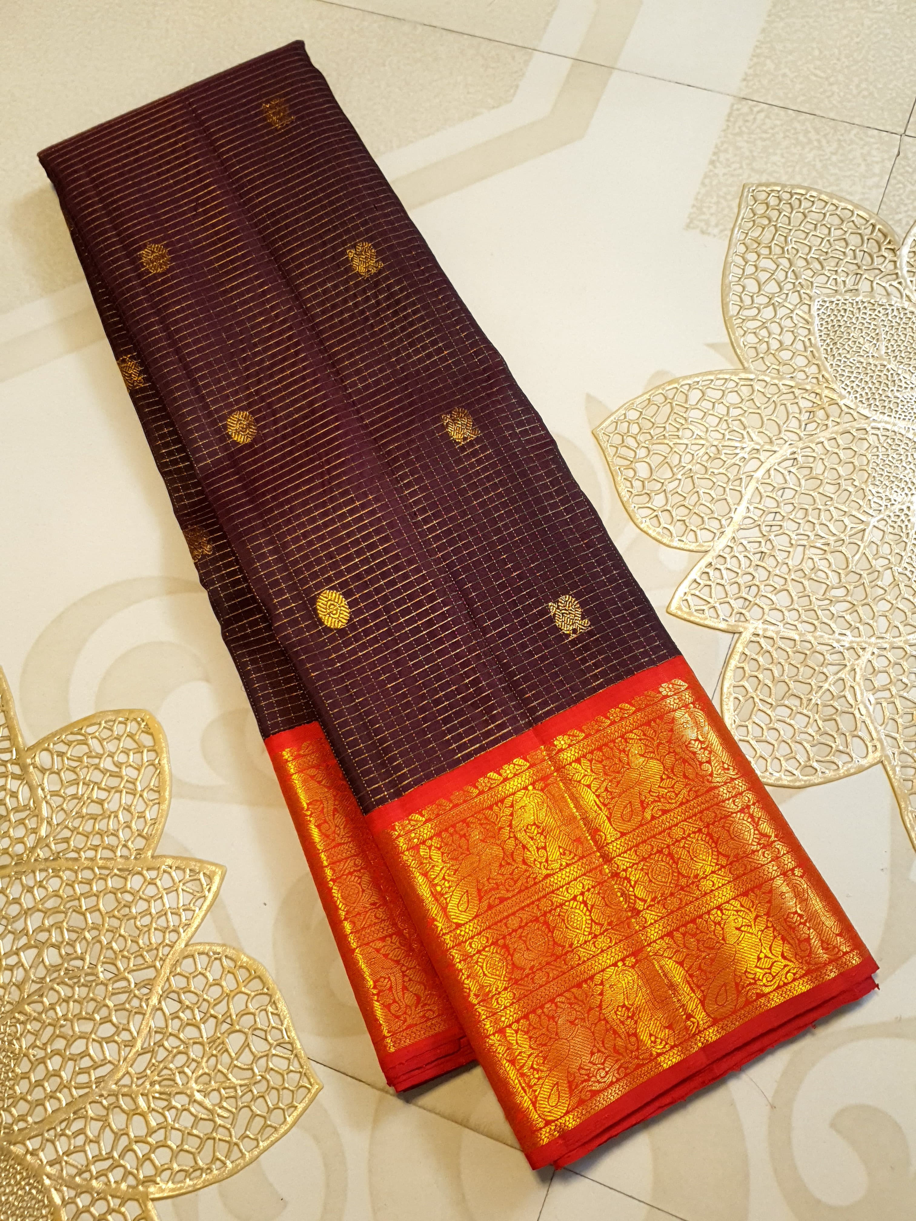 Dark plum Kanchipuram silk saree featuring a gold Muthukattam check pattern, ornate zari buttas, and a vibrant contrast border and pallu.