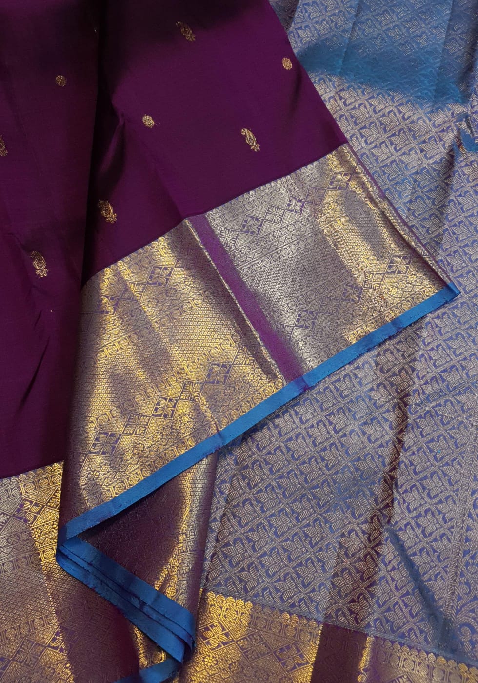 Dark plum Kanchipuram silk saree featuring a gold zari buttas, and a vibrant contrast border and pallu.
