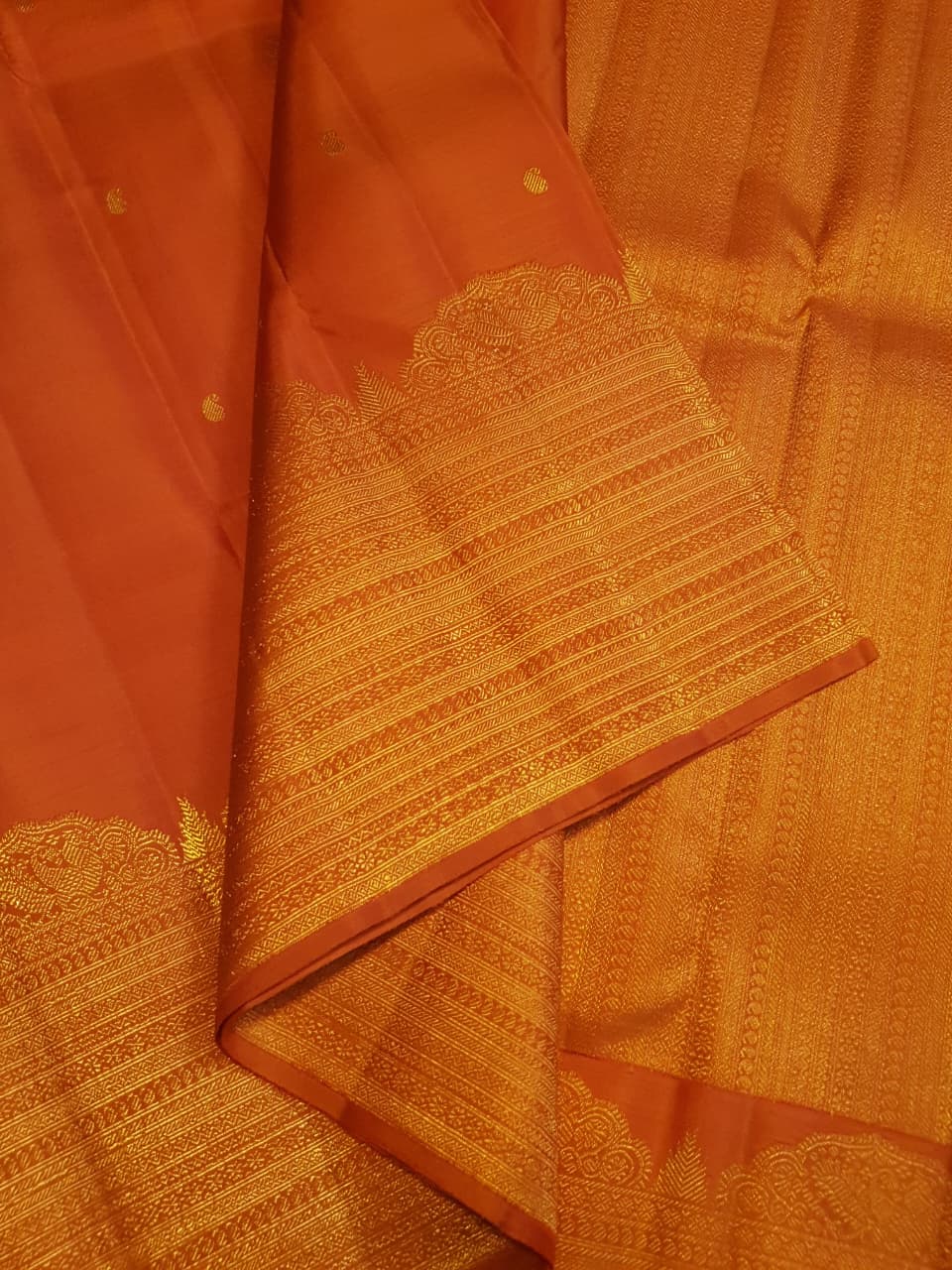 Burnt Orange Kanchipuram handloom pattu silk bridal saree featuring small gold buttas, intricate gold zari scalloped borders, and a certified silk mark weave.