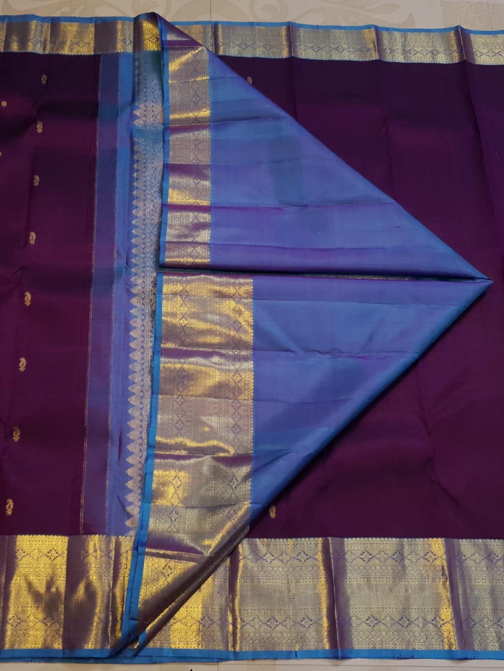 Dark plum Kanchipuram silk saree featuring a gold zari buttas, and a vibrant contrast border and pallu.