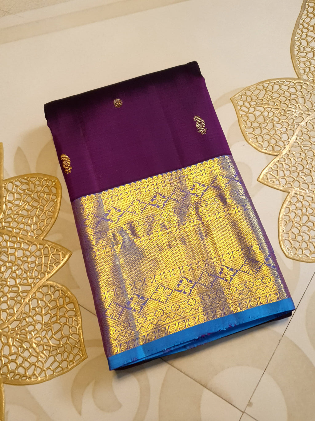 Dark plum Kanchipuram silk saree featuring a gold zari buttas, and a vibrant contrast border and pallu.