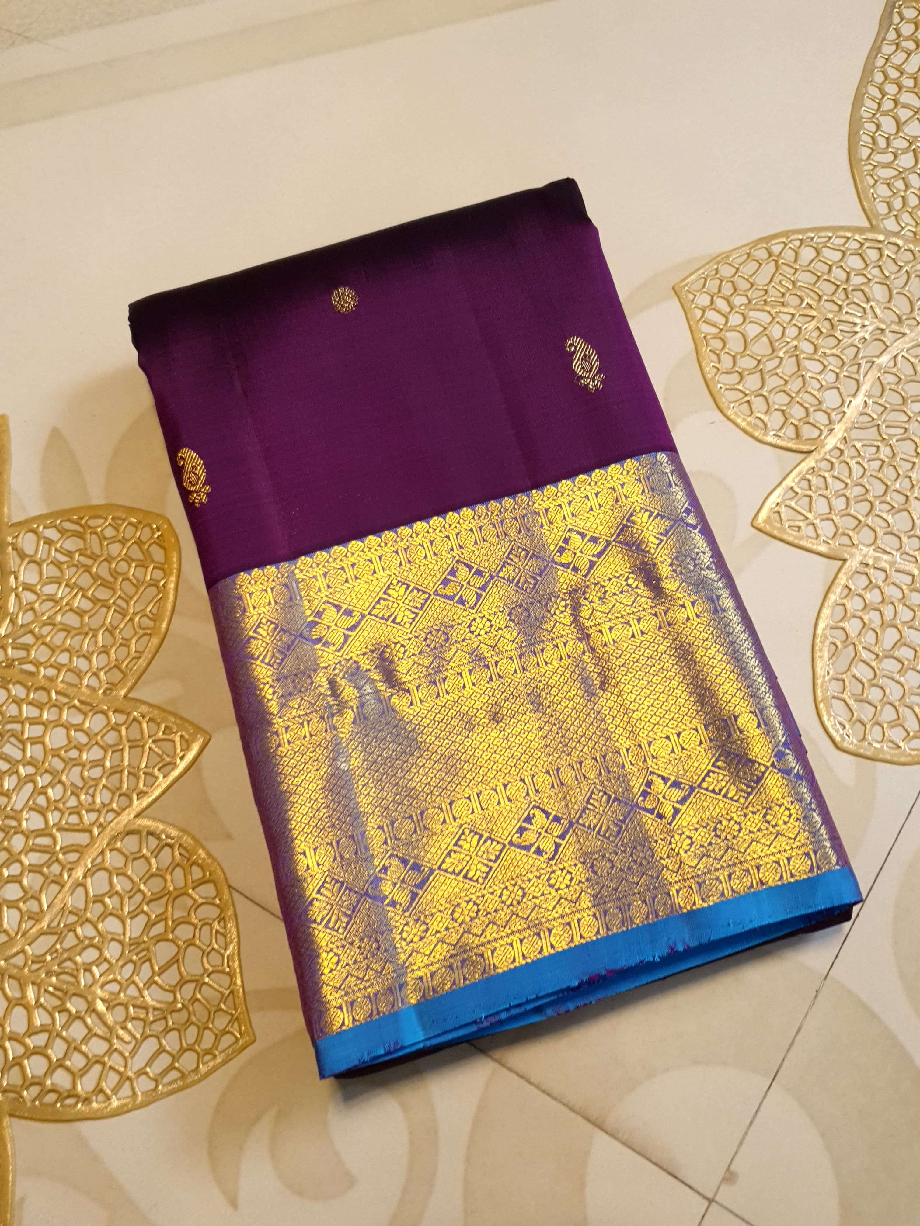 Dark plum Kanchipuram silk saree featuring a gold zari buttas, and a vibrant contrast border and pallu.