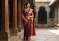 A model elegantly draped in a dark plum Kanchipuram silk saree featuring a gold Muthukattam check pattern, ornate zari buttas, and a vibrant contrast border and pallu.