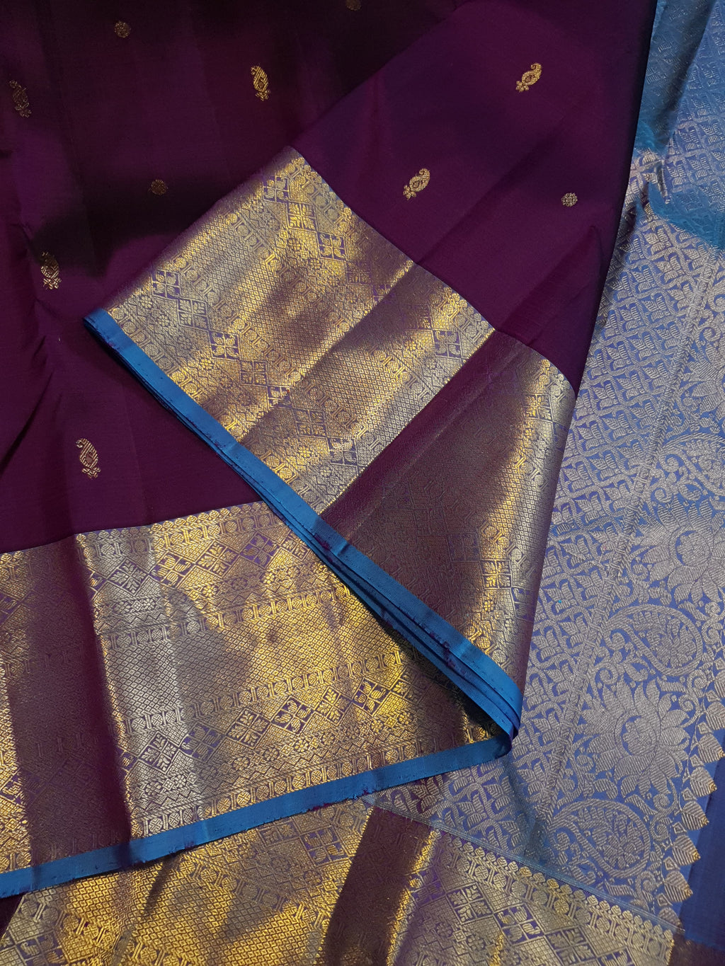 Dark plum Kanchipuram silk saree featuring a gold zari buttas, and a vibrant contrast border and pallu.