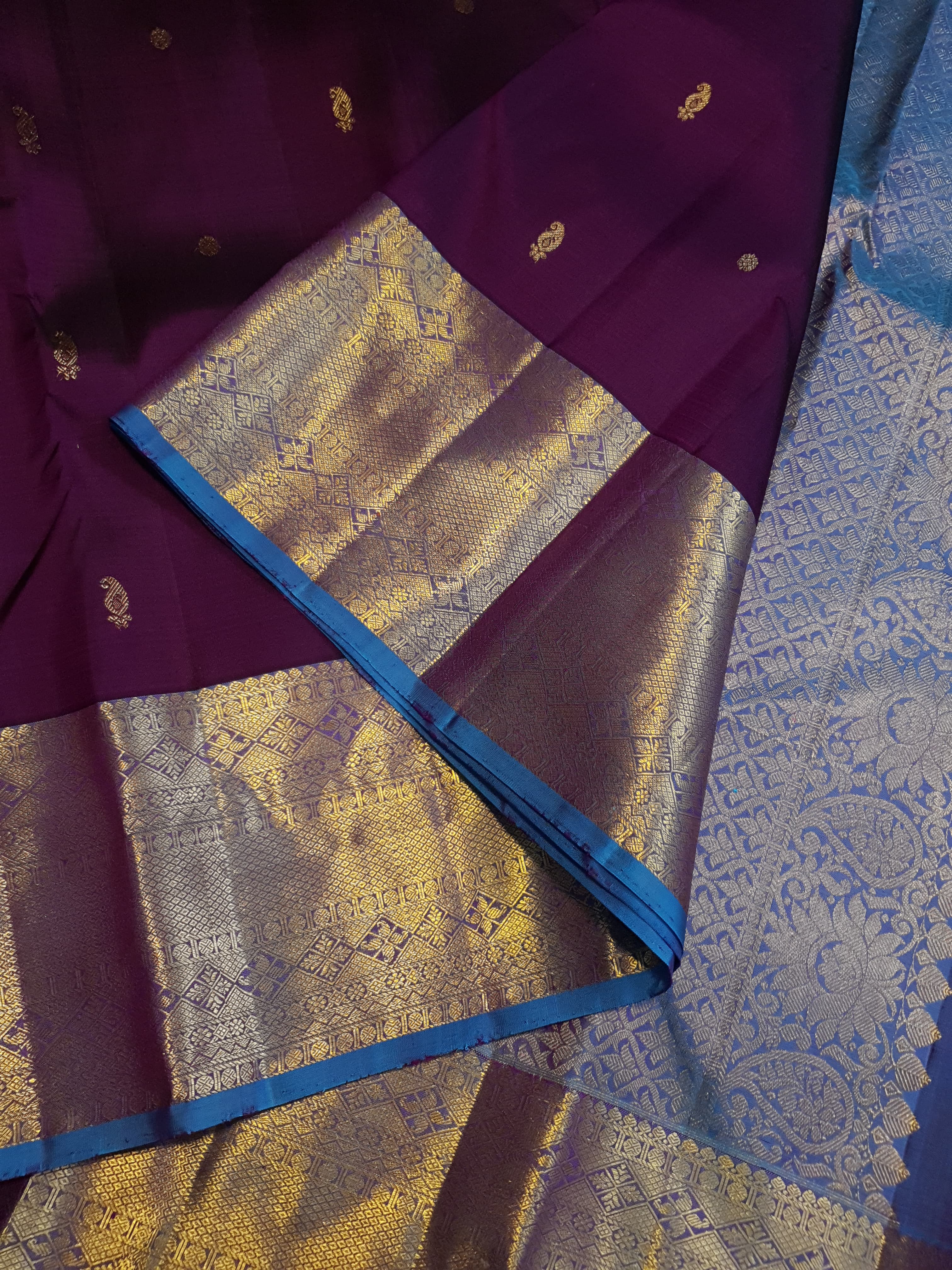 Dark plum Kanchipuram silk saree featuring a gold zari buttas, and a vibrant contrast border and pallu.