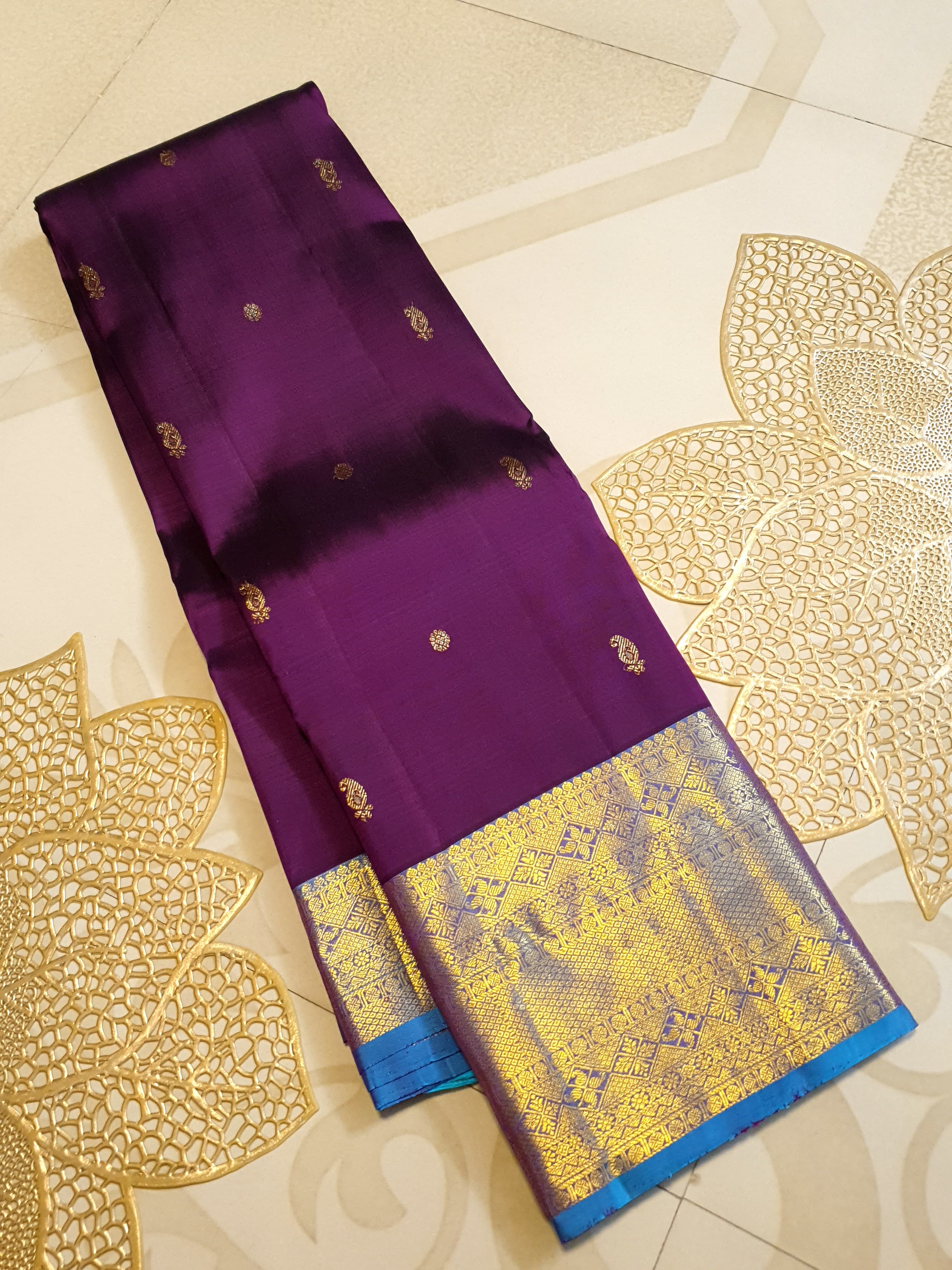 Dark plum Kanchipuram silk saree featuring a gold zari buttas, and a vibrant contrast border and pallu.