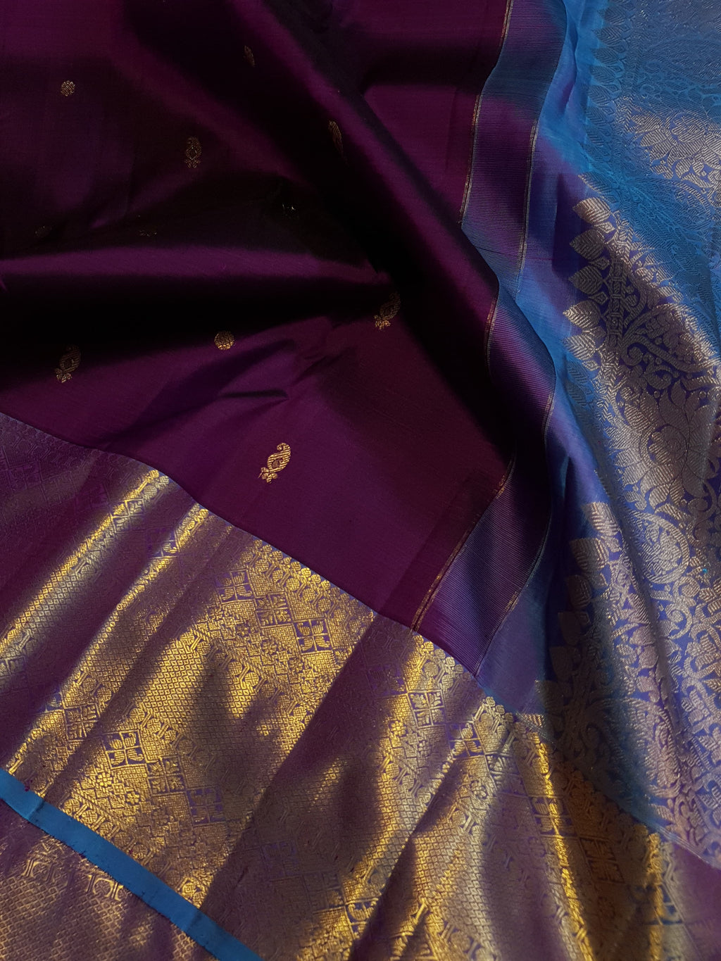 Dark plum Kanchipuram silk saree featuring a gold zari buttas, and a vibrant contrast border and pallu.