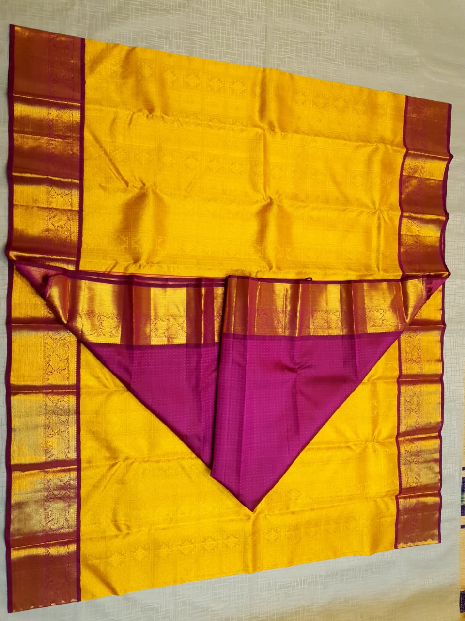 Traditional golden yellow Kanchipuram handloom 2G gold pattu silk saree with a rich magenta and zari woven border in a festive setting.