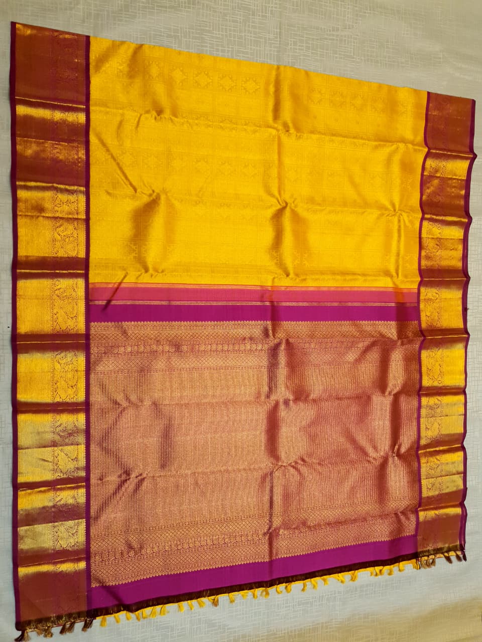 Traditional golden yellow Kanchipuram handloom 2G gold pattu silk saree with a rich magenta and zari woven border in a festive setting.