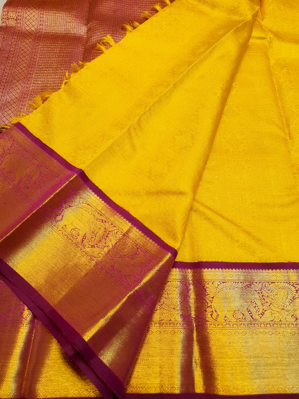 Traditional golden yellow Kanchipuram handloom 2G gold pattu silk saree with a rich magenta and zari woven border in a festive setting.