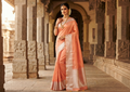 A model elegantly draped in a coral Kanchipuram handloom silk saree featuring a detailed silver zari temple border and luxurious silver accents.