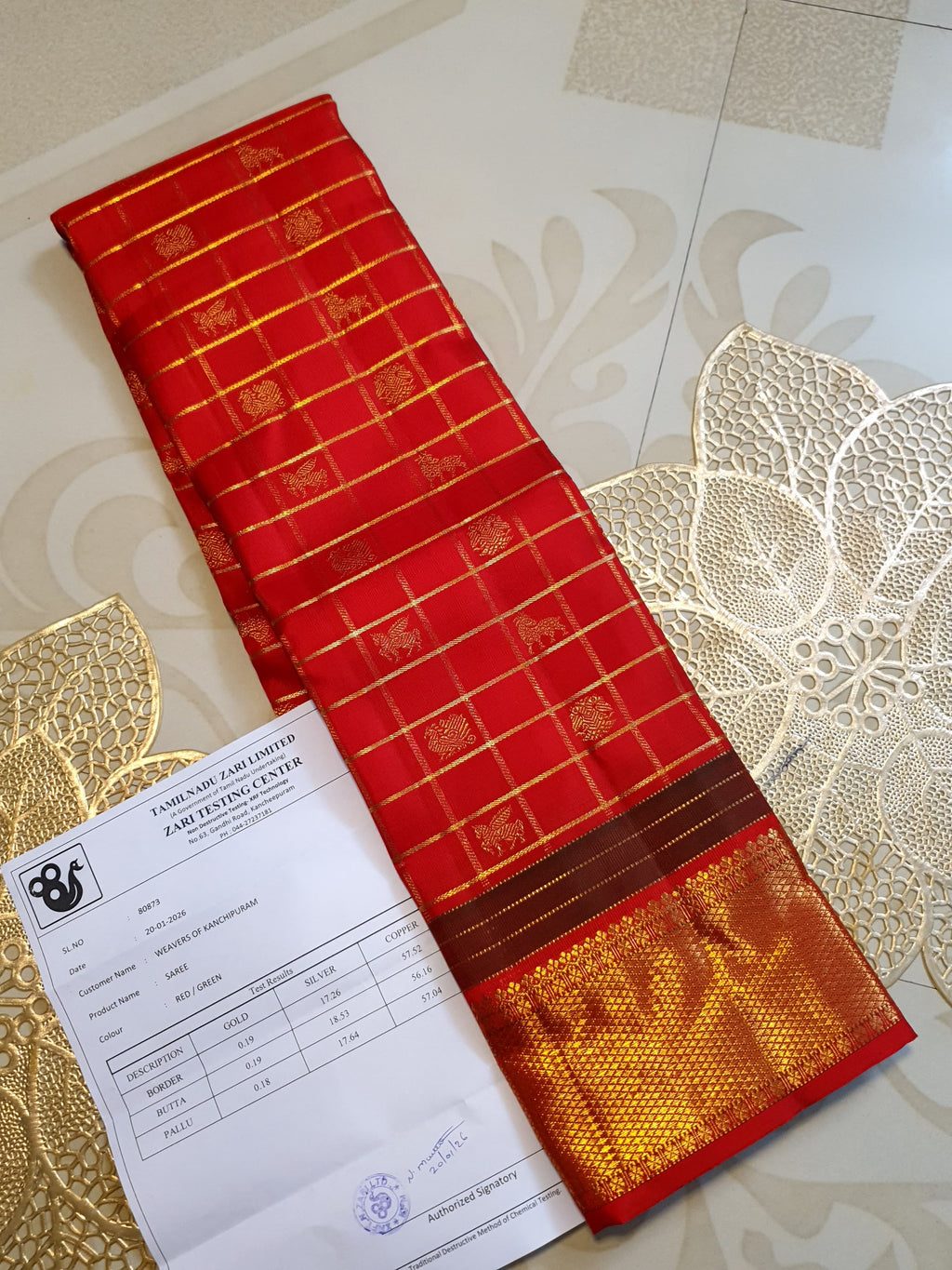 Rustic red Kanchipuram handloom silk saree featuring 3G pure gold zari checks, traditional buttas, and a rich woven border.