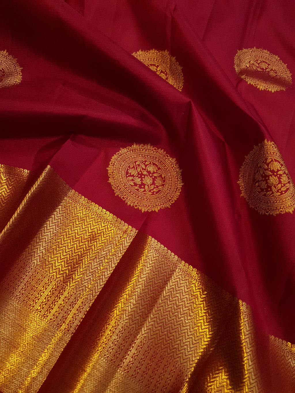 Rustic red Kanchipuram handloom pattu silk saree featuring intricate 2G gold roundel motifs, classic gold zari borders, and a certified silk mark weave.