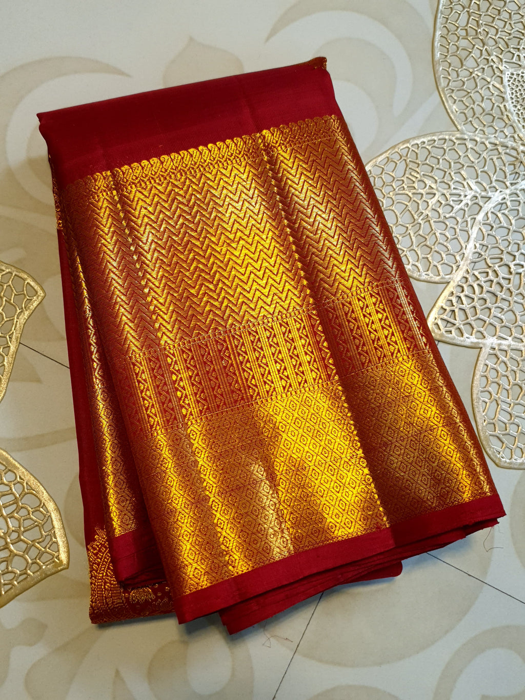 Rustic red Kanchipuram handloom pattu silk saree featuring intricate 2G gold roundel motifs, classic gold zari borders, and a certified silk mark weave.
