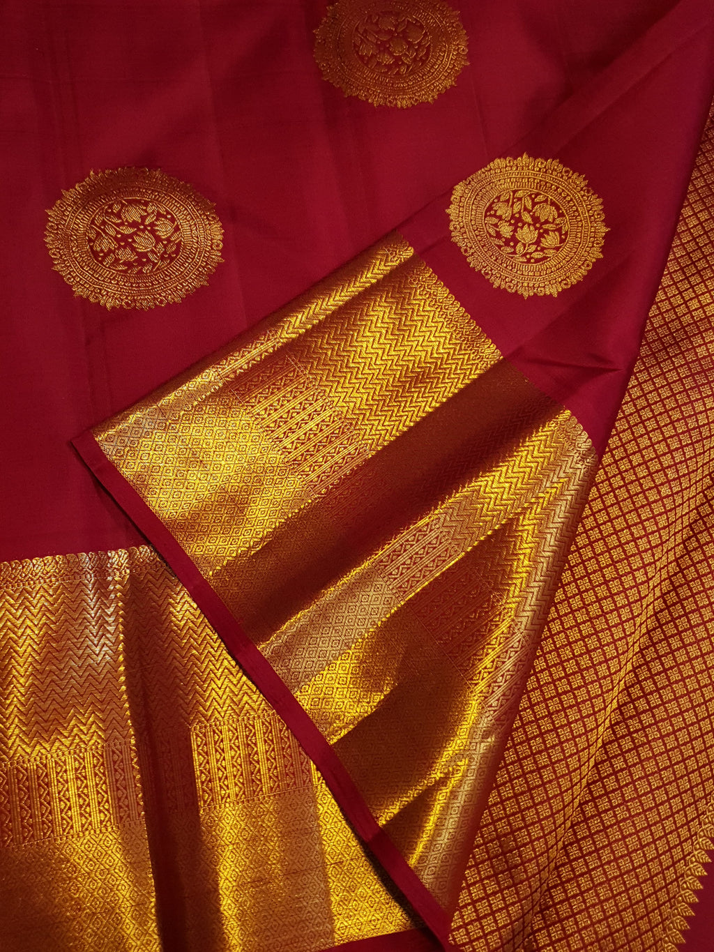 Rustic red Kanchipuram handloom pattu silk saree featuring intricate 2G gold roundel motifs, classic gold zari borders, and a certified silk mark weave.