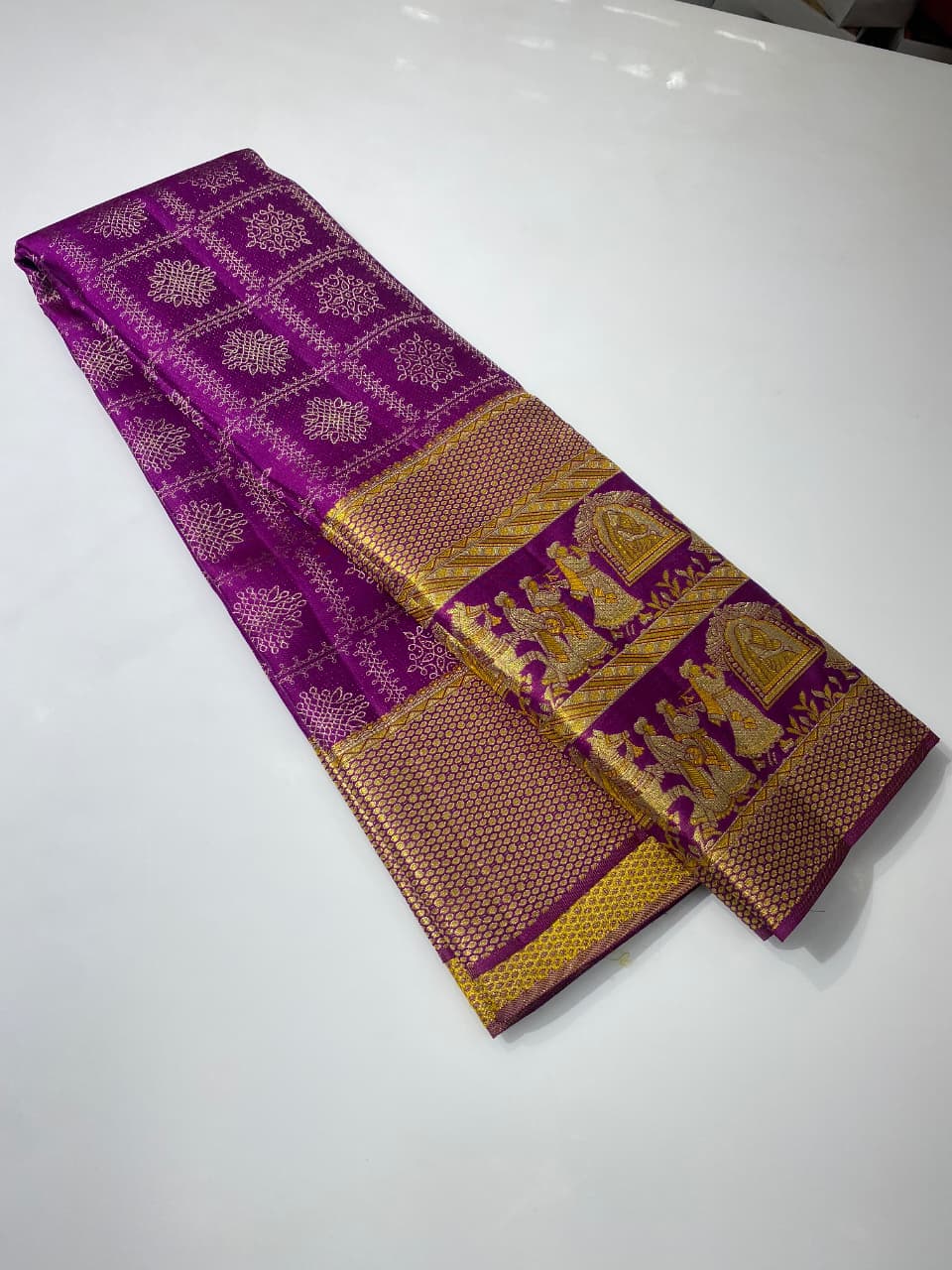 A luxurious purple Kanchipuram handloom tissue silk saree with an ornate gold zari border showcasing detailed Kalyana Pallakku (bridal palanquin) meenakari motifs.