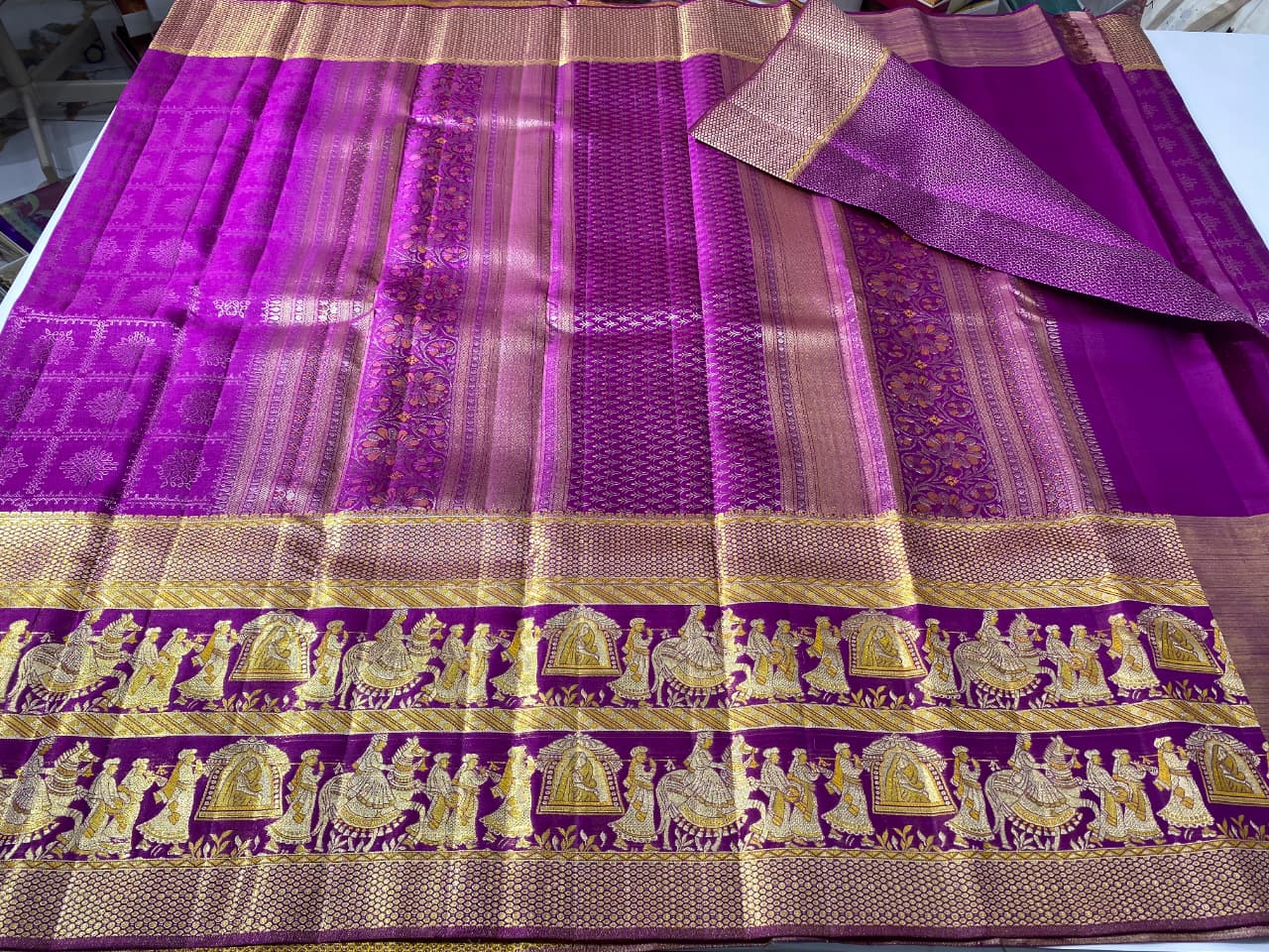 A luxurious purple Kanchipuram handloom tissue silk saree with an ornate gold zari border showcasing detailed Kalyana Pallakku (bridal palanquin) meenakari motifs.