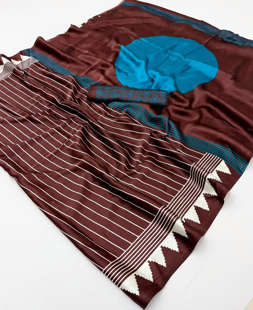 A chocolate brown modal silk saree laid flat, featuring white vertical pinstripes, a large bright teal circle on the pallu, and a matching teal patterned blouse piece.