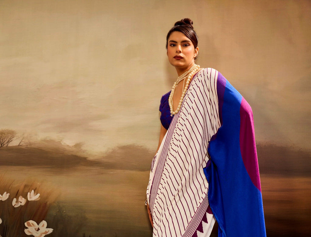 Off-white modal silk saree featuring thin maroon pinstripes, a vibrant electric blue pallu with a large maroon circle, and a maroon sawtooth geometric border.