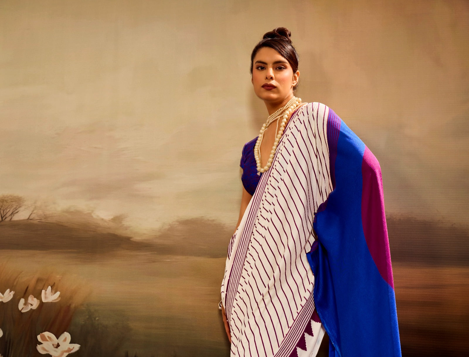 Off-white modal silk saree featuring thin maroon pinstripes, a vibrant electric blue pallu with a large maroon circle, and a maroon sawtooth geometric border.