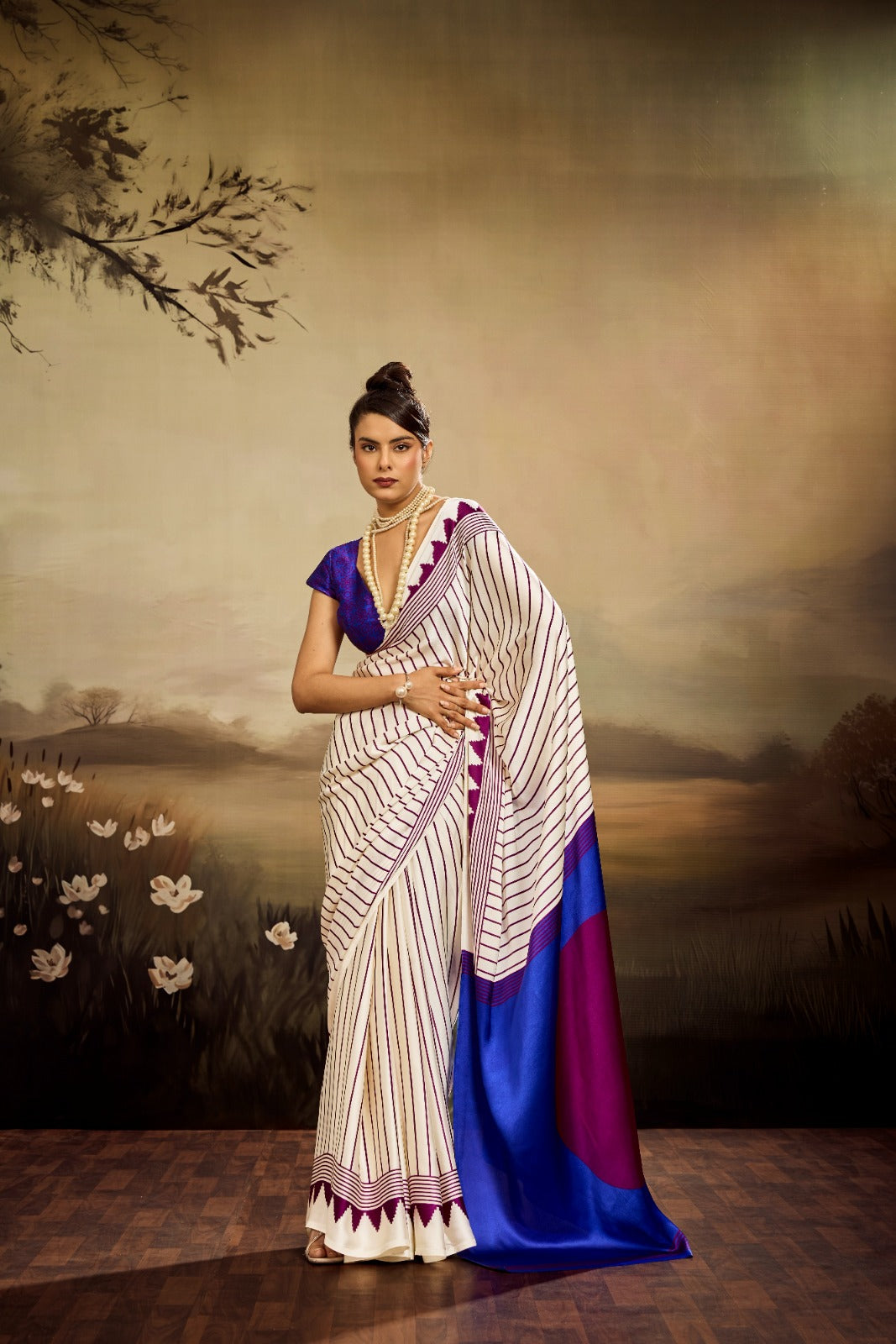 Off-white modal silk saree featuring thin maroon pinstripes, a vibrant electric blue pallu with a large maroon circle, and a maroon sawtooth geometric border.