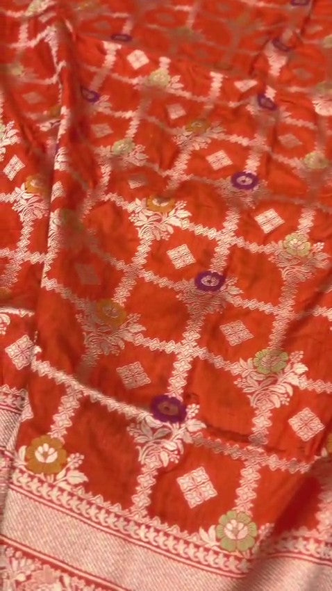 A vibrant orange handloom Banarasi Katan silk saree with an intricate all-over grid pattern and multicolored Meenakari floral motifs, featuring a heavy gold zari border and pallu.