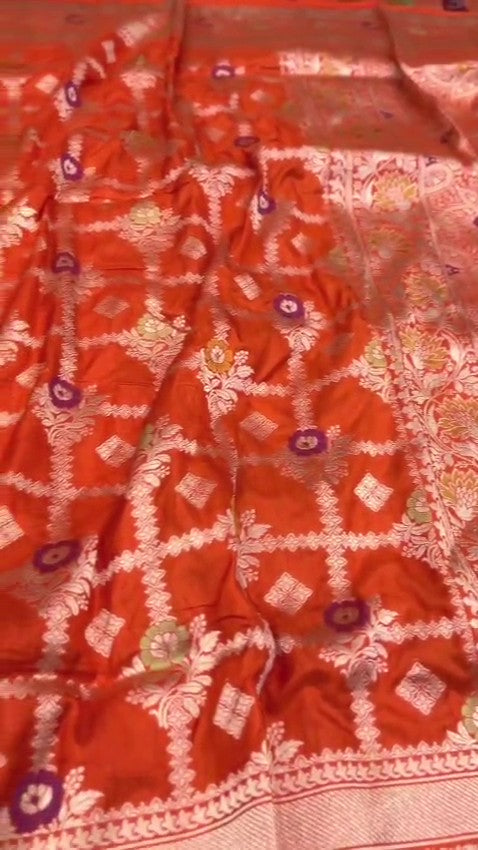 A vibrant orange handloom Banarasi Katan silk saree with an intricate all-over grid pattern and multicolored Meenakari floral motifs, featuring a heavy gold zari border and pallu.