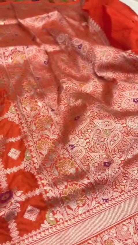 A vibrant orange handloom Banarasi Katan silk saree with an intricate all-over grid pattern and multicolored Meenakari floral motifs, featuring a heavy gold zari border and pallu.