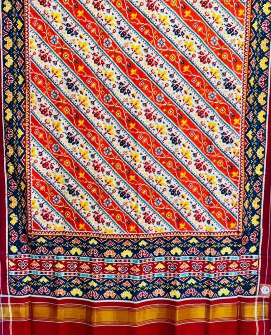 A magnificent coral Patan Patola double ikat pure mulberry silk saree featuring vibrant diagonal multi-colored geometric patterns, intricate contrasting borders, and a rich traditional pallu dyed with natural vegetable colors.
