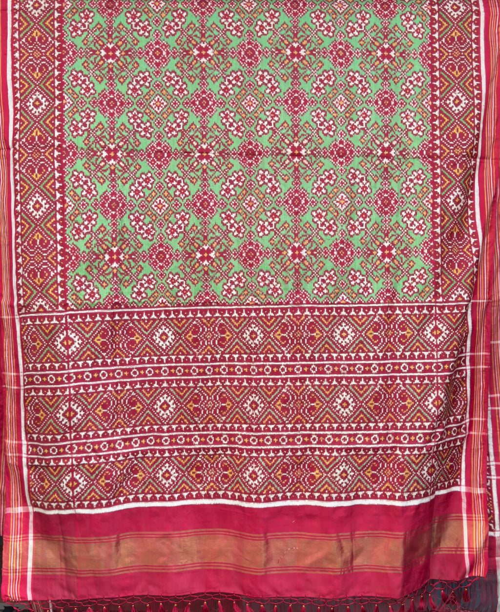 A striking green Patan Patola double ikat pure mulberry silk saree featuring intricate red and white geometric patterns, ornate contrasting borders, and a magnificent rich red pallu dyed using natural vegetable colors.