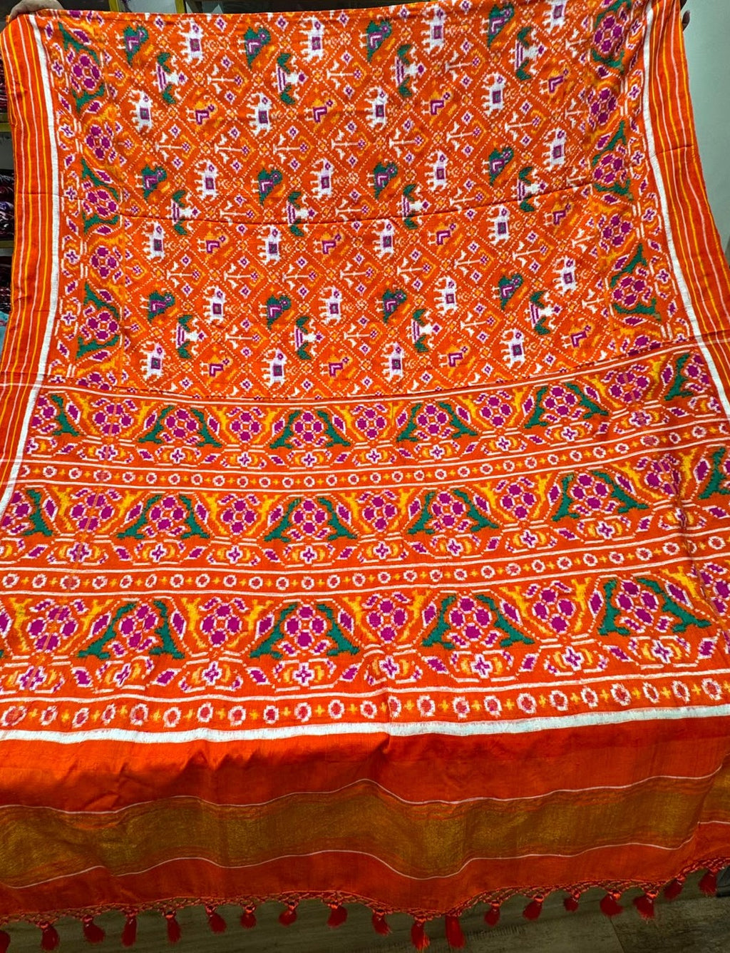 A vibrant orange Patan Patola double ikat pure mulberry silk saree featuring intricate multicolored elephant and geometric motifs, striking floral pallu panels, and traditional borders.