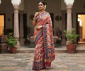 A magnificent coral Patan Patola double ikat pure mulberry silk saree featuring vibrant diagonal multi-colored geometric patterns, intricate contrasting borders, and a rich traditional pallu dyed with natural vegetable colors.