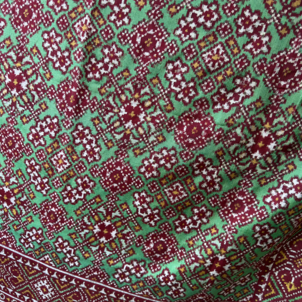 A striking green Patan Patola double ikat pure mulberry silk saree featuring intricate red and white geometric patterns, ornate contrasting borders, and a magnificent rich red pallu dyed using natural vegetable colors.