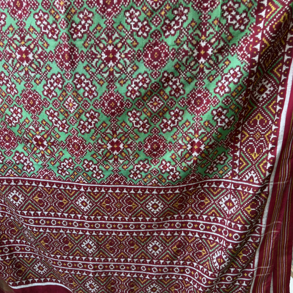 A striking green Patan Patola double ikat pure mulberry silk saree featuring intricate red and white geometric patterns, ornate contrasting borders, and a magnificent rich red pallu dyed using natural vegetable colors.