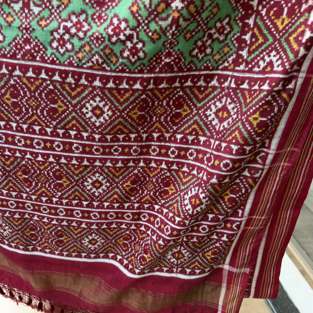 A striking green Patan Patola double ikat pure mulberry silk saree featuring intricate red and white geometric patterns, ornate contrasting borders, and a magnificent rich red pallu dyed using natural vegetable colors.