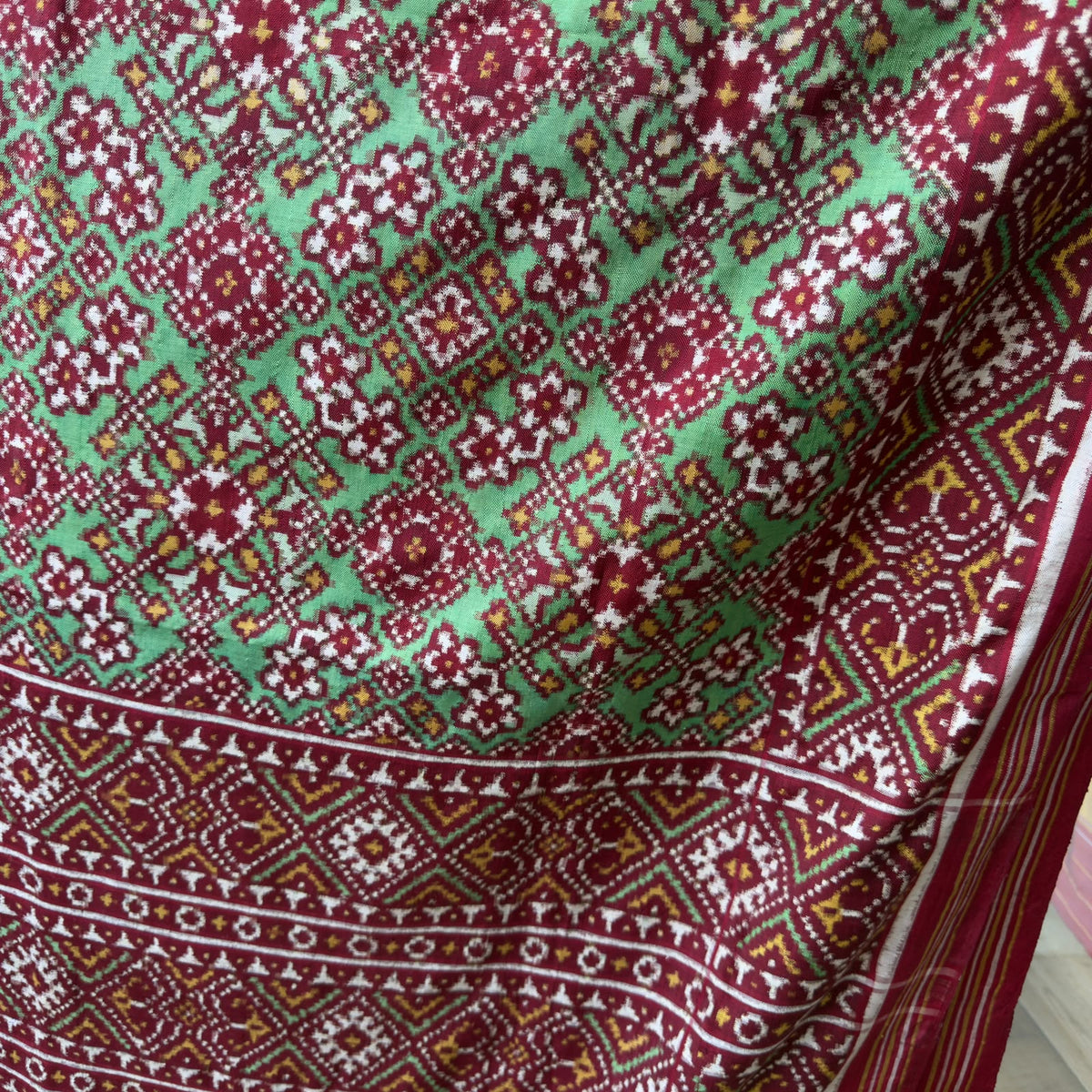 A striking green Patan Patola double ikat pure mulberry silk saree featuring intricate red and white geometric patterns, ornate contrasting borders, and a magnificent rich red pallu dyed using natural vegetable colors.