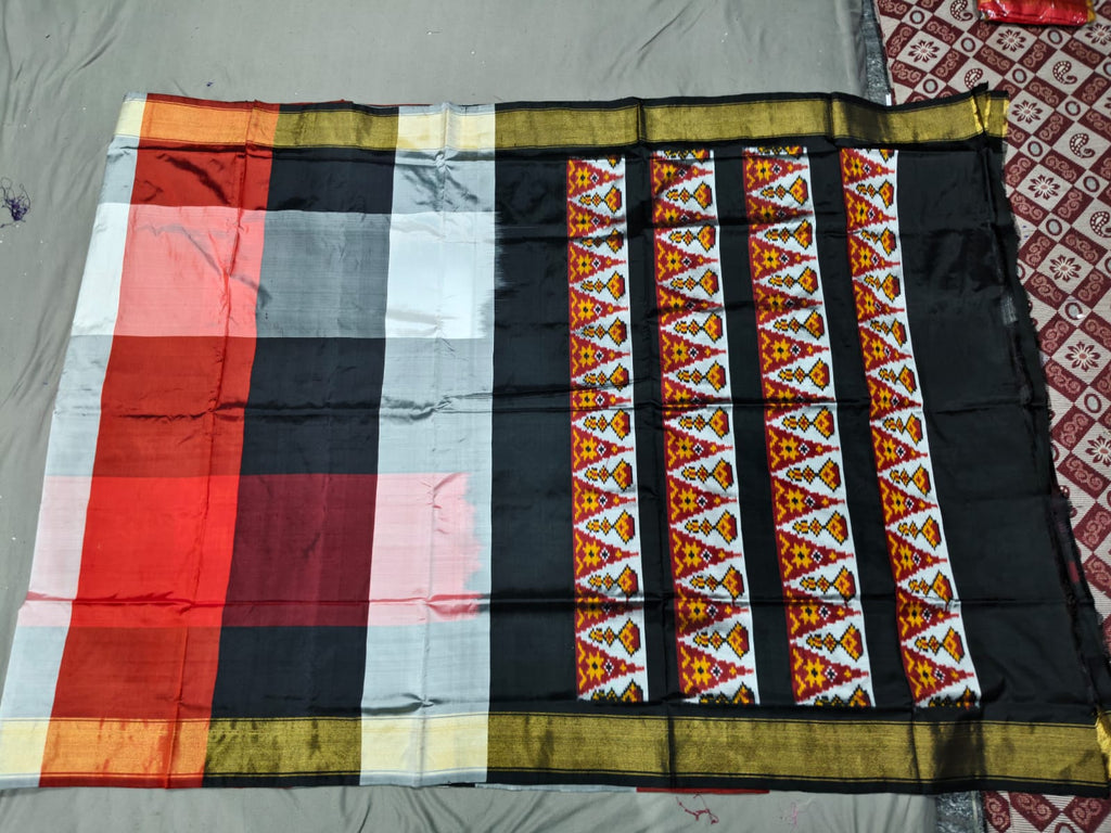 A premium red, white, and black Pochampally handloom silk saree showcasing authentic geometric Ikkat patterns, a solid contrasting border, and a Silk Mark certified assurance tag.