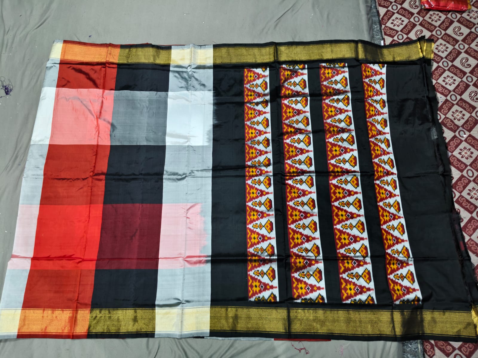 A premium red, white, and black Pochampally handloom silk saree showcasing authentic geometric Ikkat patterns, a solid contrasting border, and a Silk Mark certified assurance tag.