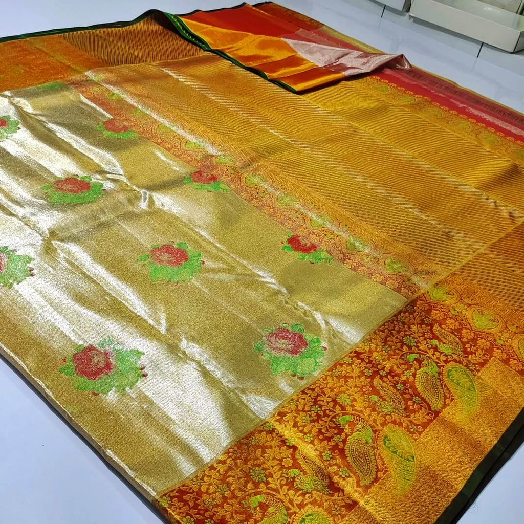 A close-up of a luxurious gold tissue Kanchipuram silk saree with vibrant rust orange borders and intricate Meenakari floral brocade weaving.