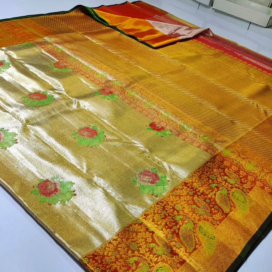 A close-up of a luxurious gold tissue Kanchipuram silk saree with vibrant rust orange borders and intricate Meenakari floral brocade weaving.