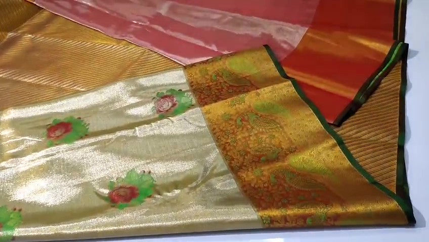 A close-up of a luxurious gold tissue Kanchipuram silk saree with vibrant rust orange borders and intricate Meenakari floral brocade weaving.