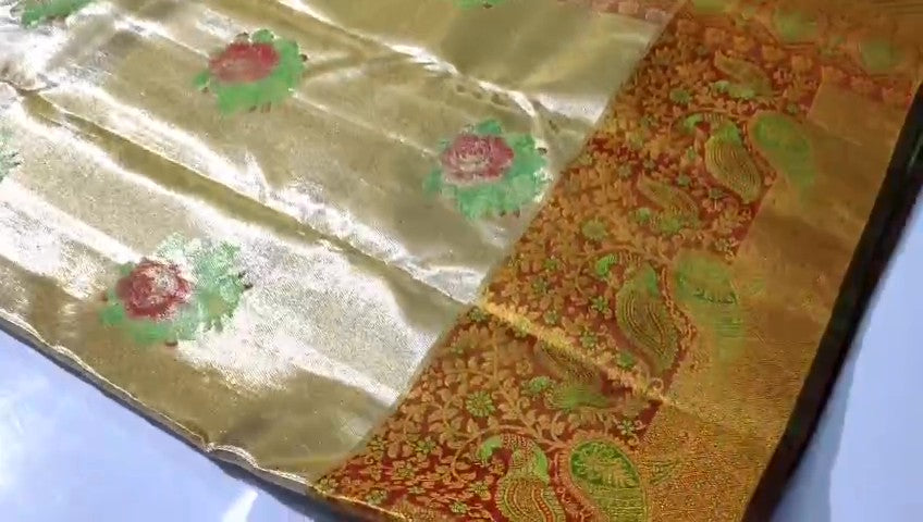 A close-up of a luxurious gold tissue Kanchipuram silk saree with vibrant rust orange borders and intricate Meenakari floral brocade weaving.