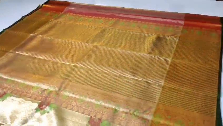 A close-up of a luxurious gold tissue Kanchipuram silk saree with vibrant rust orange borders and intricate Meenakari floral brocade weaving.