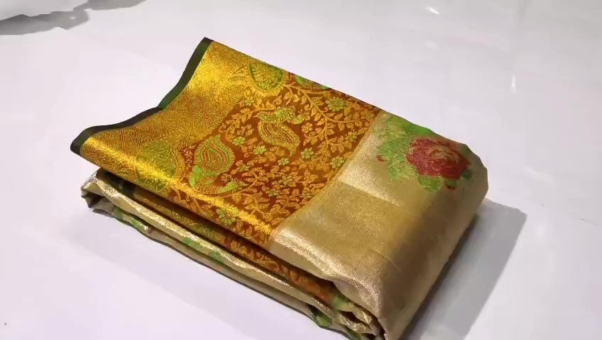 A close-up of a luxurious gold tissue Kanchipuram silk saree with vibrant rust orange borders and intricate Meenakari floral brocade weaving.