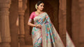 A woman wearing a luxurious turquoise Kanchipuram handloom tissue brocade Meenakari silk saree with intricate floral motifs and a pink contrast border.
