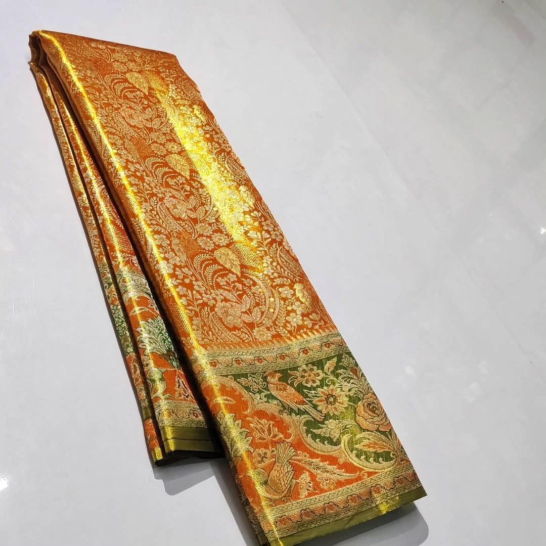 Dual-tone Orange and gold Kanchipuram tissue brocade silk saree featuring intricate Meenakari floral and bird motifs, styled with a contrasting olive green blouse in a traditional temple corridor.